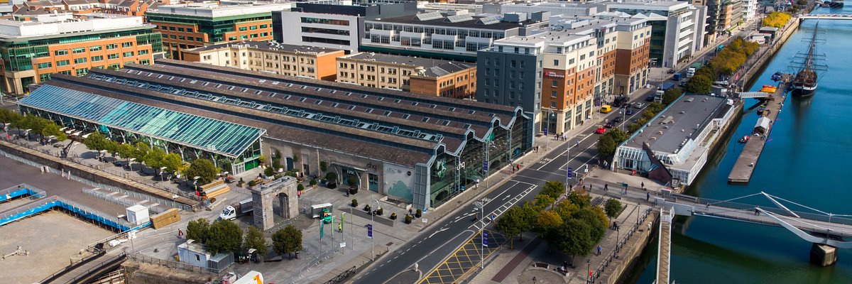 Aerial view of our Dublin office featuring a contemporary glass building with tree-lined exterior, surrounded by urban architecture near the River Liffey.